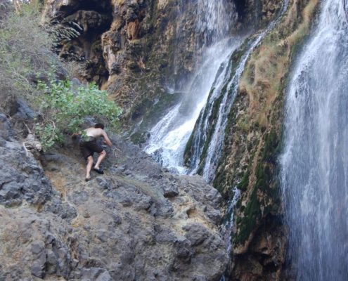 Met slippers op steile rotsen klimmen zoals deze avontuurlijke safarigast is niet nodig om de Ngare Sero watervallen in het Natron-meer te bereiken.
